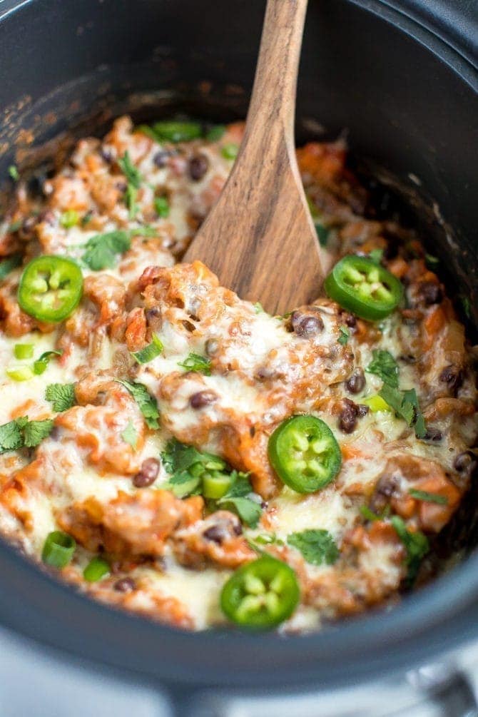 Vegetarian Mexican quinoa casserole in a slow cooker topped with melted cheese, sliced jalapeno, green onions and cilantro.