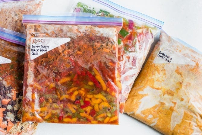 4 freezer bags with vegetarian freezer meals. Freezer meals include vegetarian chili, sweet and sour tempeh, Mexican quinoa bake, and red lentil butternut stew.