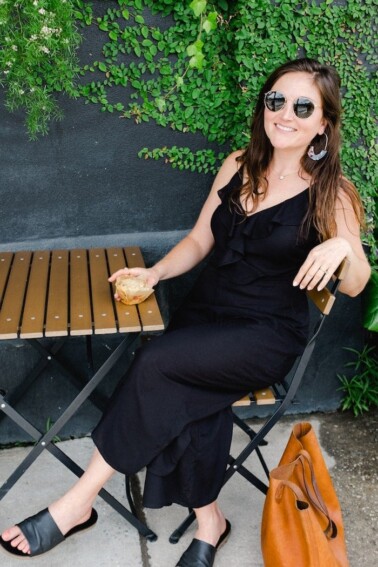 Woman in black sitting at an outdoor table with a baked good in her hand.