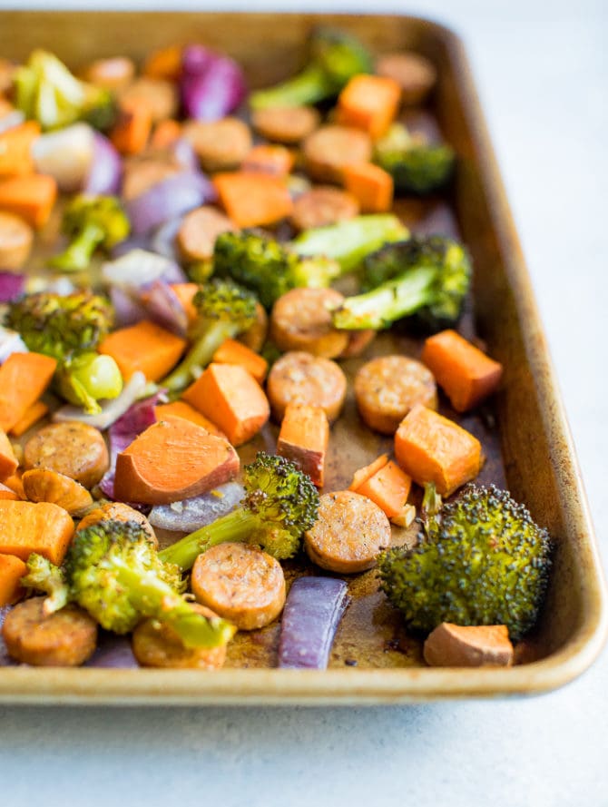 Sheet pan with roasted chicken sausage, red onion, broccoli, and sweet potato.