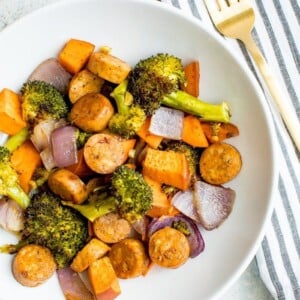 Sausage, broccoli, butternut squash and onion on a white plate.