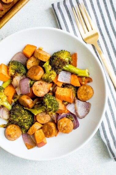 Sausage, broccoli, butternut squash and onion on a white plate.