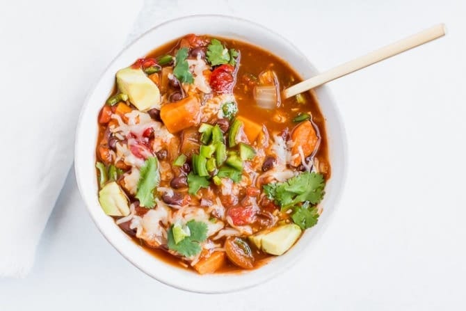 Slow cooker sweet potato and black bean vegetarian chili in a bowl topped with cilantro, cheese and jalapeño.