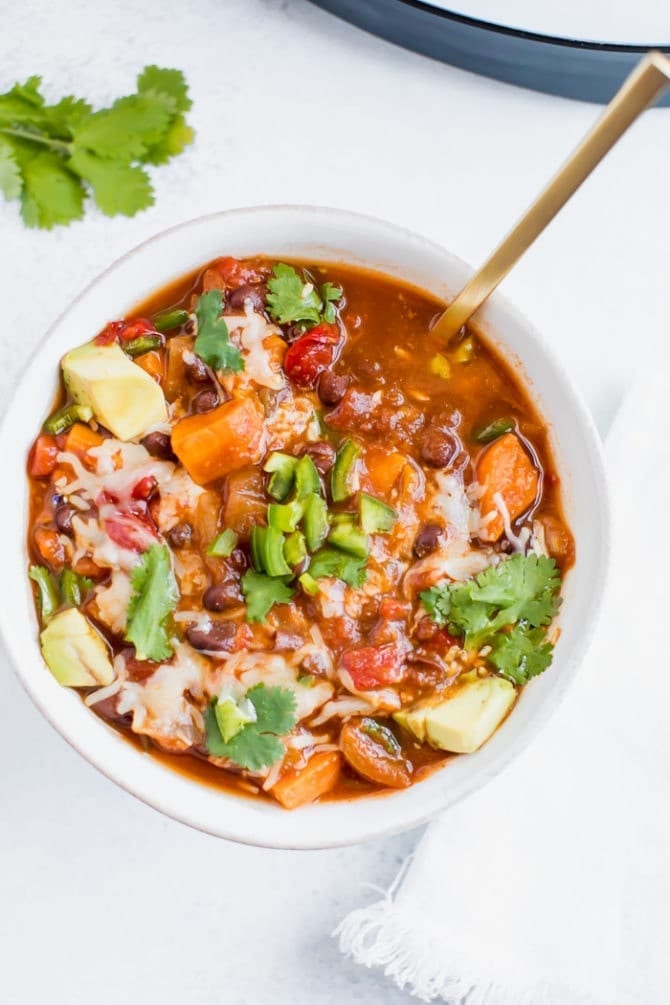 Slow cooker sweet potato and black bean vegetarian chili in a bowl topped with cilantro, cheese and jalapeรฑo.