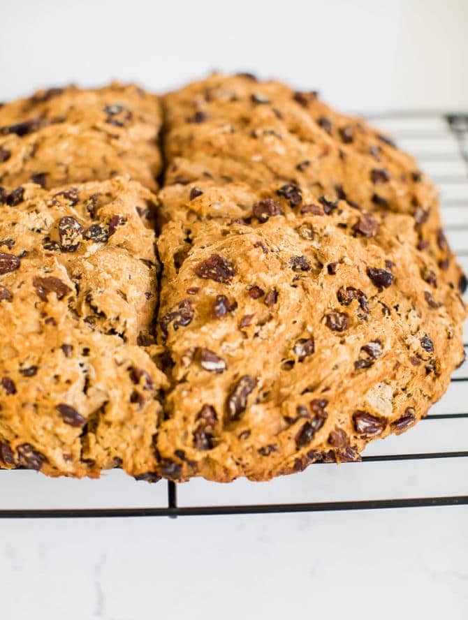 Irish soda bread made which whole wheat and raisins. Loaf is resting on a wire cooling rack.