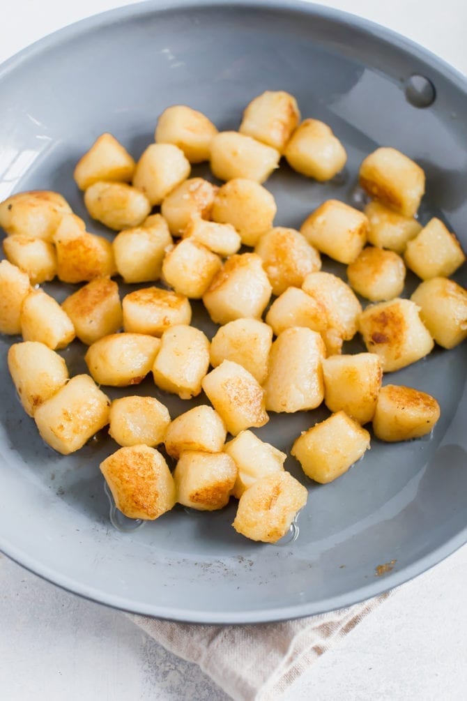 Trader Joe's cauliflower gnocchi sautéing in a skillet with olive oil.