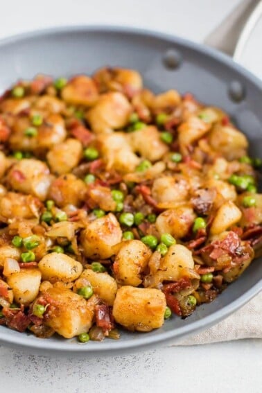 Skillet of Trader Joe's cauliflower gnocchi, sautéed with onions, peas, and turkey bacon.