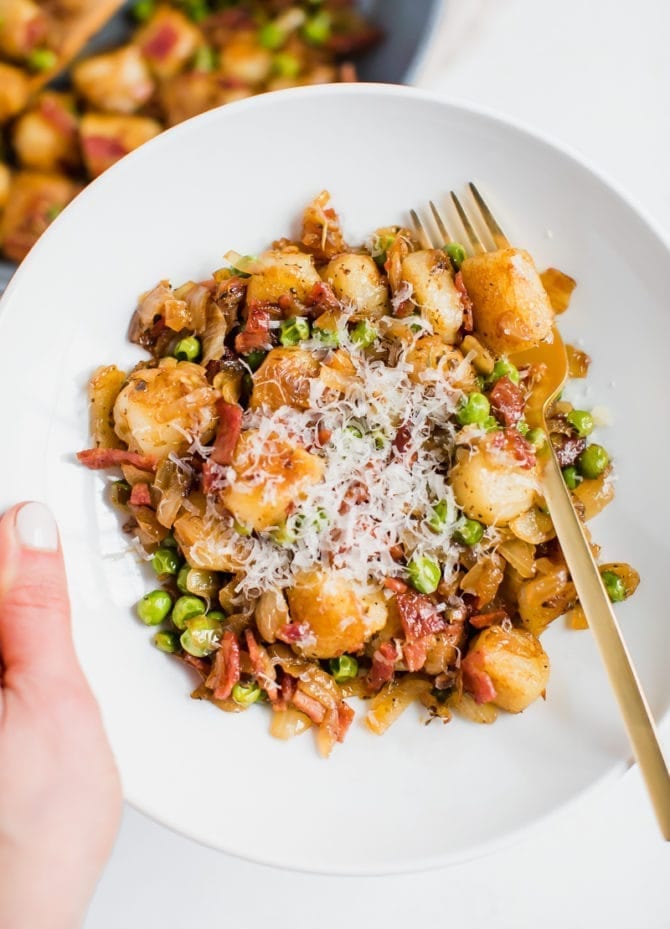 Plated cauliflower gnocchi sautéed with onions, peas and turkey bacon. Topped with parmesan cheese.