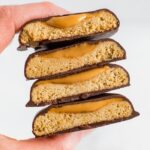 Hand holding a stack of homemade, healthy, vegan and gluten-free Tagalong cookies. Almond flour shortbread cookie, topped with peanut butter and coated with chocolate.