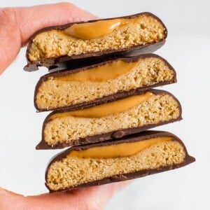 Hand holding a stack of homemade, healthy, vegan and gluten-free Tagalong cookies. Almond flour shortbread cookie, topped with peanut butter and coated with chocolate.