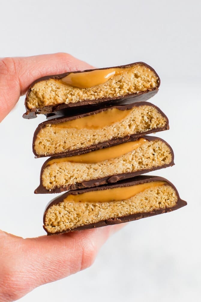 Hand holding a stack of homemade, healthy, vegan and gluten-free Tagalong cookies. Almond flour shortbread cookie, topped with peanut butter and coated with chocolate.