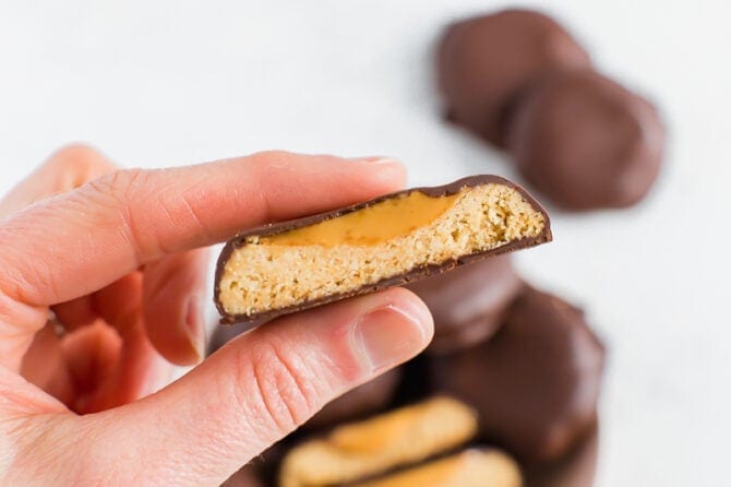Hand holding a homemade healthy Tagalong cookie. Shortbread cookie topped with peanut butter and covered in chocolate.