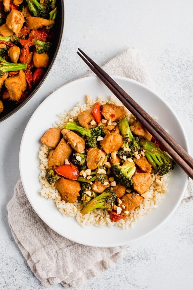 Healthy Kung Pao chicken with peppers, broccoli and chopped peanuts with rice in a bowl with chopsticks.