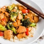 Kung pao chicken over rice with vegetables and peanuts on a plate with chopsticks.