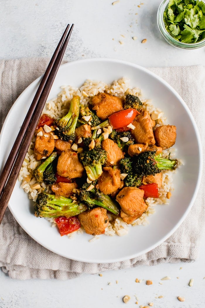 Healthy Kung Pao chicken with peppers, broccoli and chopped peanuts with rice in a bowl with chopsticks.