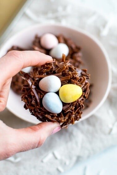 A hand holding a chocolate coconut flake Easter nest treat with Cadbury eggs in the nest.