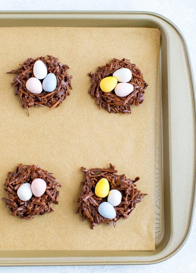 Chocolate coconut flake Easter nest treats with Cadbury eggs in the nest. Four nests on a cookie sheet lined with parchment paper.