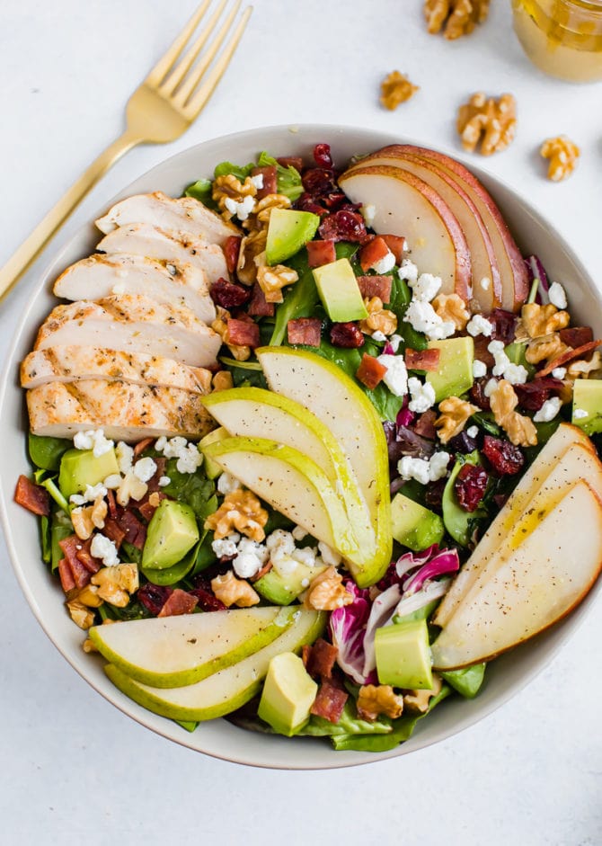 Salad topped with pears, grilled chicken, turkey bacon, cranberries, goat cheese, walnuts, and avocado.