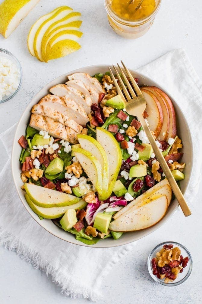 Salad topped with pears, grilled chicken, turkey bacon, cranberries, goat cheese, walnuts, and avocado.