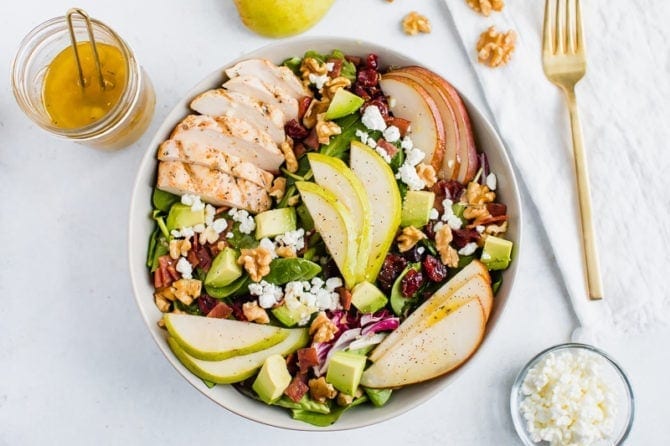 Salad topped with pears, grilled chicken, turkey bacon, cranberries, goat cheese, walnuts, and avocado.