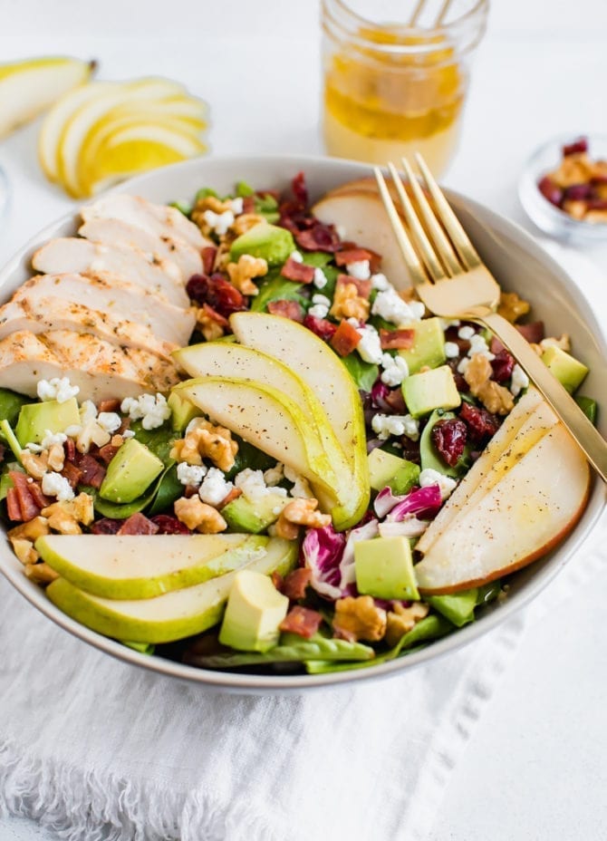 Salad topped with pears, grilled chicken, turkey bacon, cranberries, goat cheese, walnuts, and avocado.