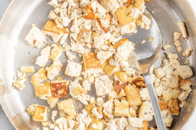 Sautéed crumbled tofu in a pan with a spoon.