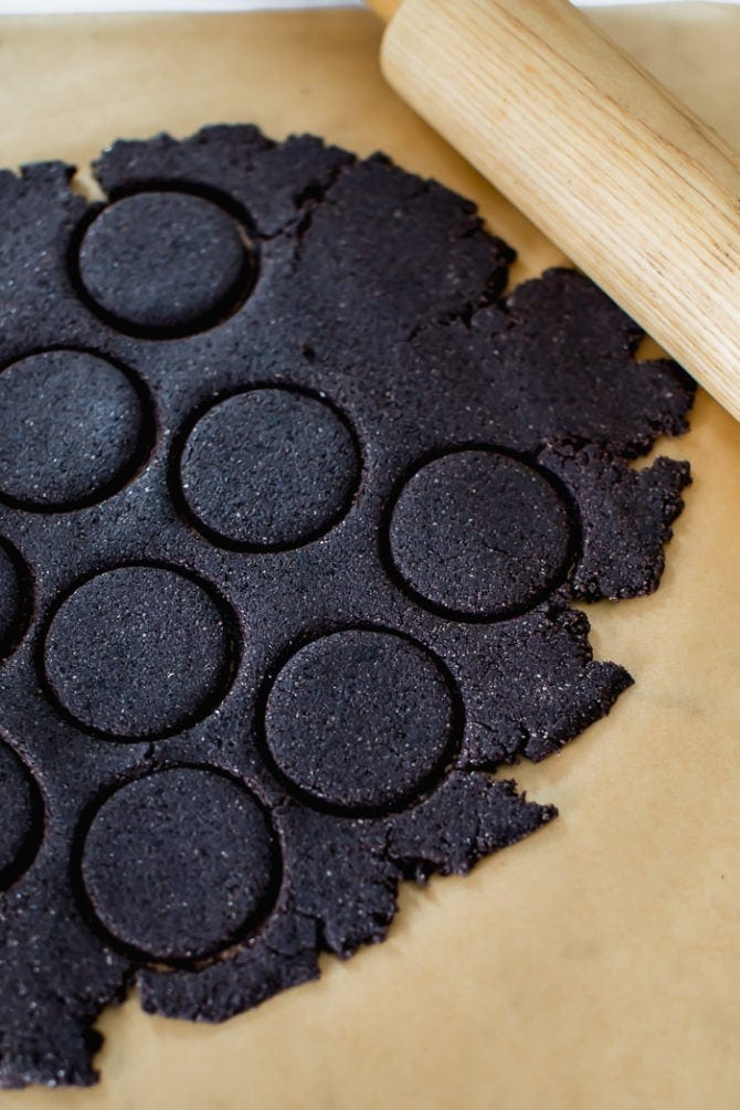Chocolate almond flour cookie dough rolled out and cut into circular shapes for cookies.