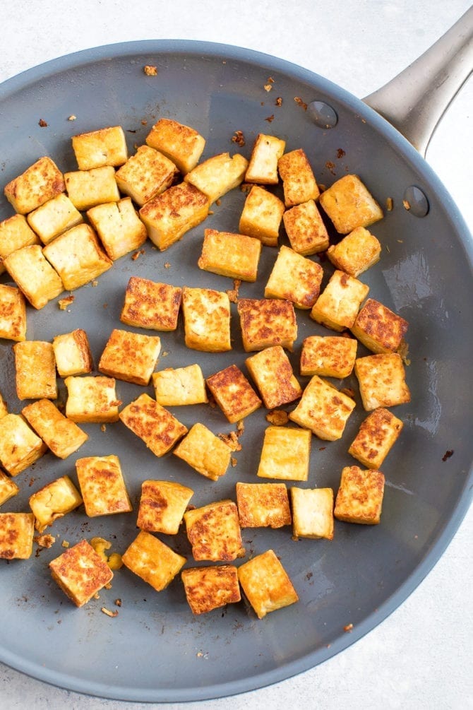 Golden, pan-fried tofu in a blue ceramic pan. 