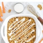 Carrot cake baked oatmeal in a baking dish drizzled with cream cheese frosting.