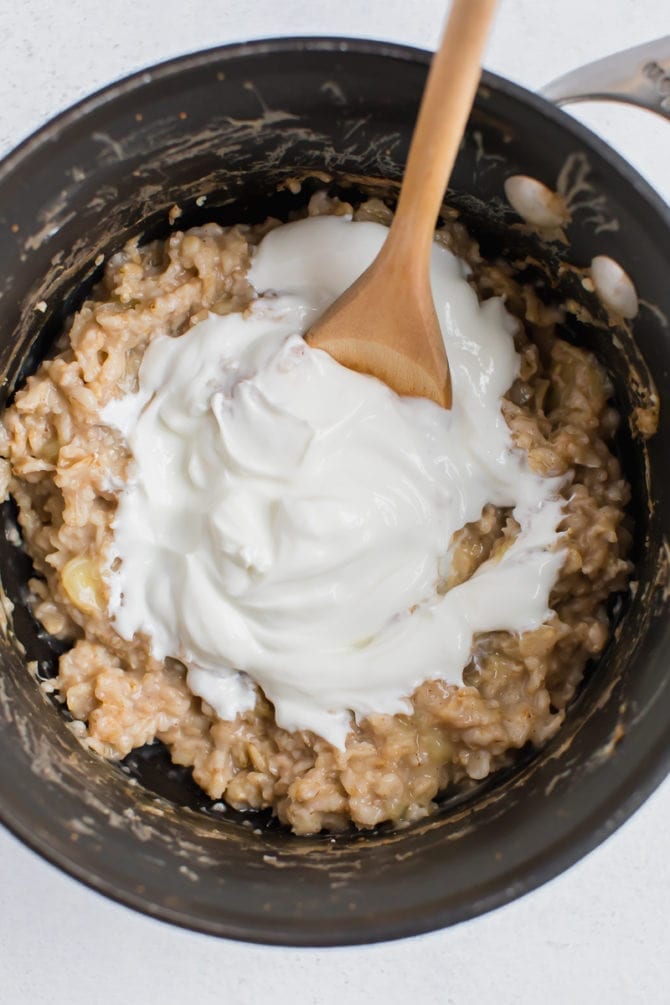 Oatmeal in a pot with a spoon mixing in plain Greek yogurt.