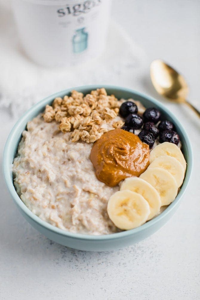 Bowl of protein greek yogurt oatmeal topped with granola, blueberries, banana slices, and peanut butter.