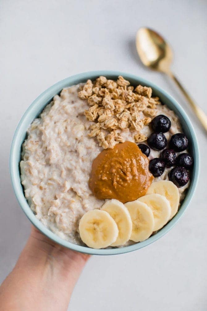 Bowl of protein greek yogurt oatmeal topped with granola, blueberries, banana slices, and peanut butter.