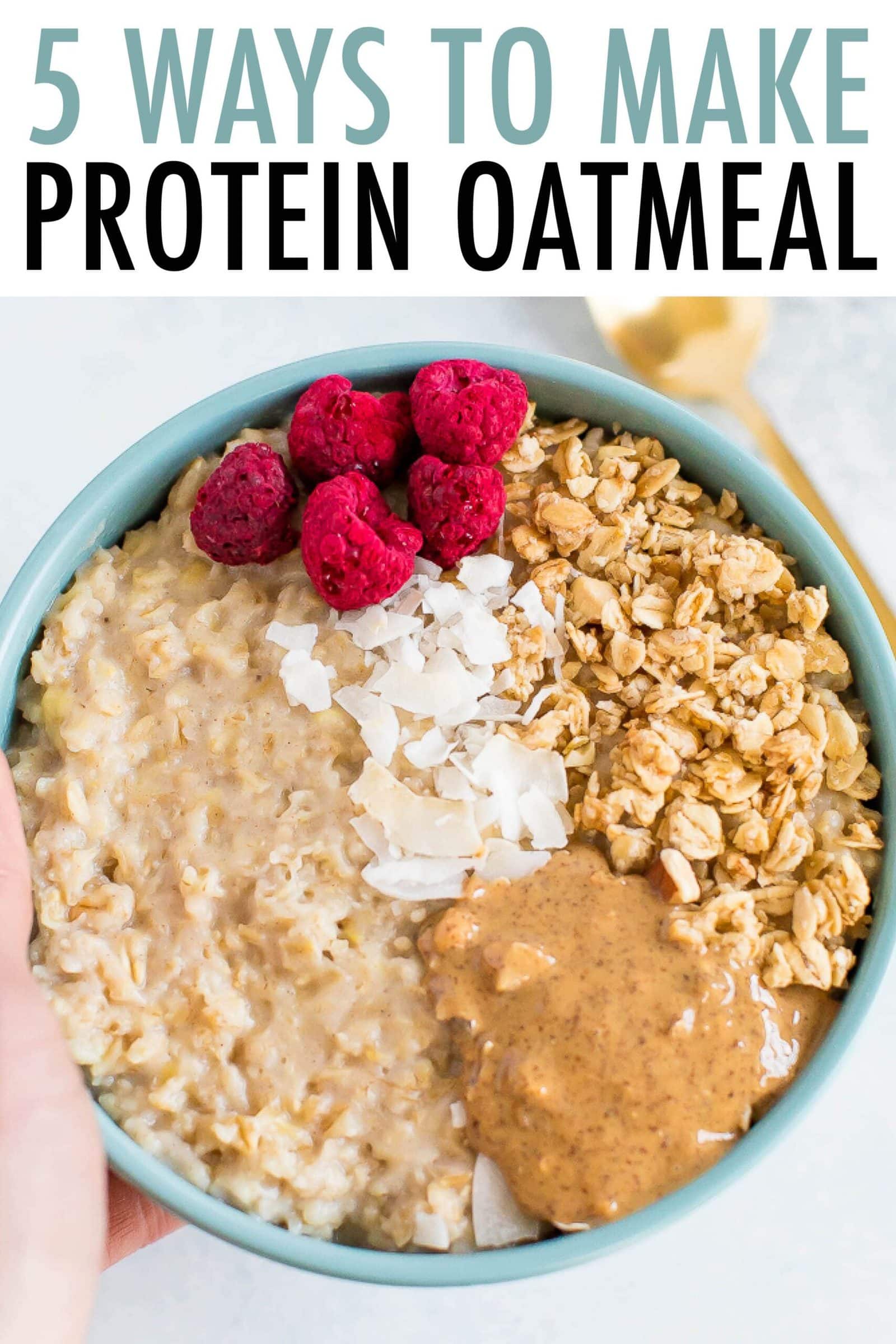 Hand holding a bowl of oatmeal topped with raspberries, granola, peanut butter and coconut.
