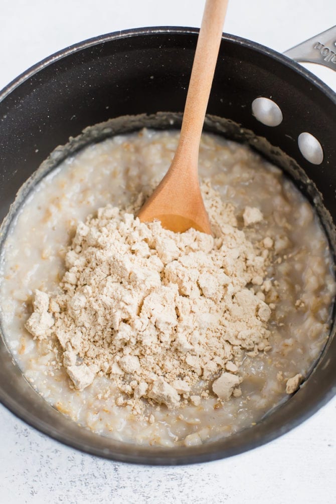 Oatmeal in a pot with a spoon mixing in vanilla protein powder.