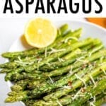 Plate of roasted asparagus topped with parmesan, red pepper flakes, and a lemon wedge on the side. Beside the bowl are smaller bowls filled with red pepper, parmesan, and a cutting board with lemon slices.