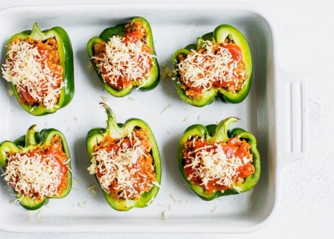 Six stuffed peppers in a baking dish. Peppers stuffed with turkey, rice, onions and tomato sauce, topped with cheese.