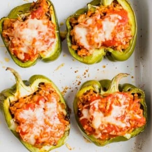 Four stuffed peppers in a baking dish. Peppers stuffed with turkey, rice, onions and tomato sauce, topped with cheese.