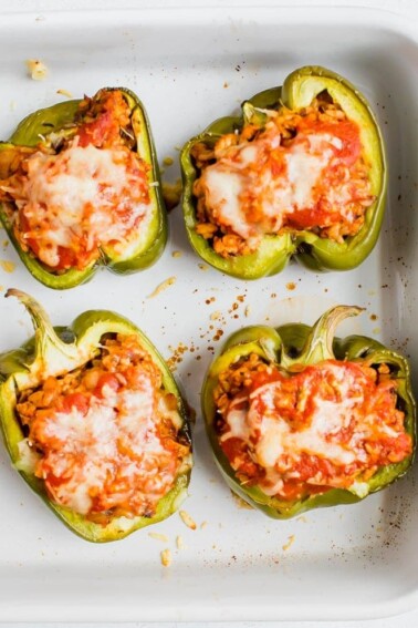 Four stuffed peppers in a baking dish. Peppers stuffed with turkey, rice, onions and tomato sauce, topped with cheese.