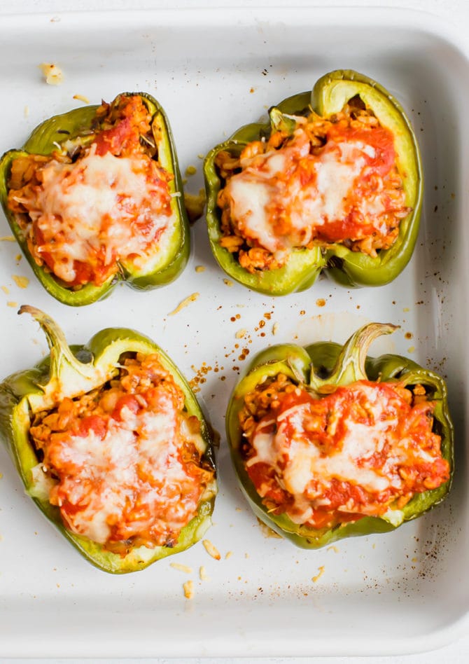 Four stuffed peppers in a baking dish. Peppers stuffed with turkey, rice, onions and tomato sauce, topped with cheese.