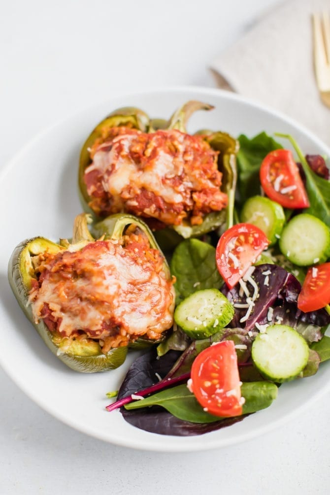 Two turkey stuffed peppers on a plate with a green salad.