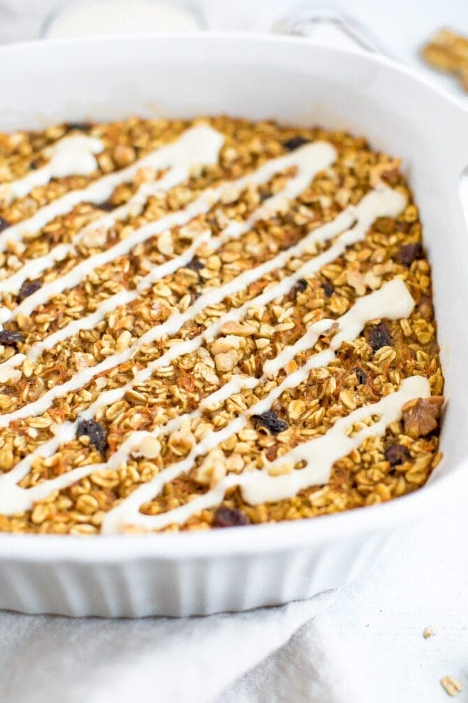 Carrot cake baked oatmeal in a baking dish drizzled with cream cheese frosting.