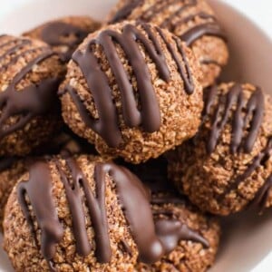 Bowl of chocolate coconut macaroons drizzled with chocolate in a white bowl.