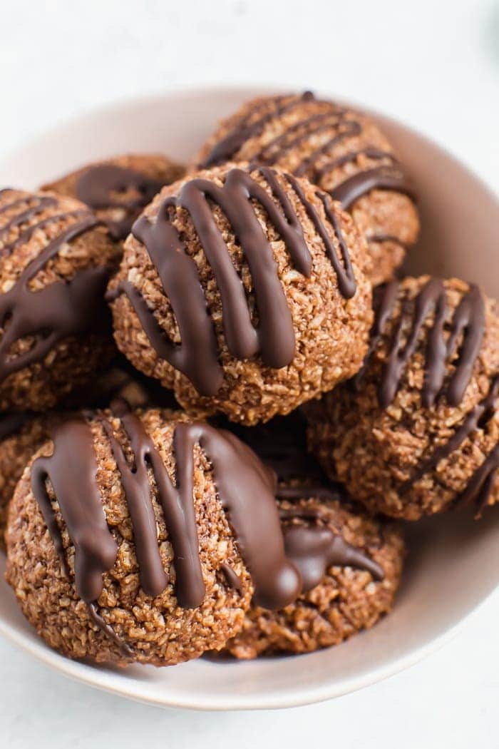 Bowl of chocolate coconut macaroons drizzled with chocolate in a white bowl.