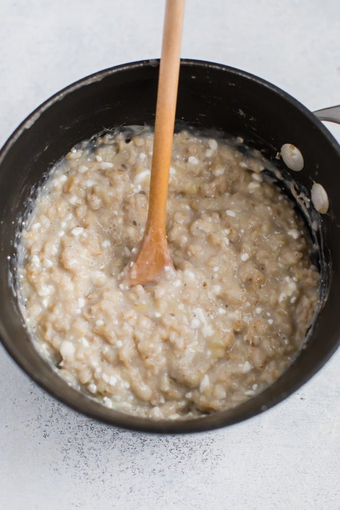 Pot of oatmeal with cottage cheese stirred in with a spoon.