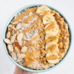 Cottage cheese oatmeal topped with almond slices, coconut flakes, banana slices, and drizzled with nut butter.