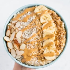 Cottage cheese oatmeal topped with almond slices, coconut flakes, banana slices, and drizzled with nut butter.