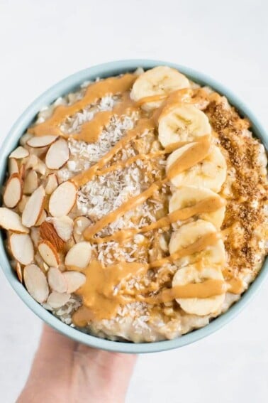 Cottage cheese oatmeal topped with almond slices, coconut flakes, banana slices, and drizzled with nut butter.