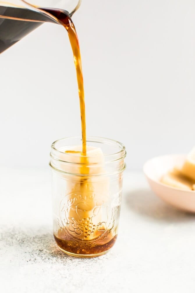 Cold brew being poured into a mason jar with almondmilk creamer ice cubes.