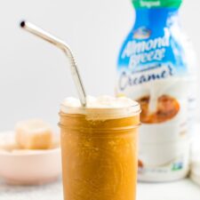 Almond Breeze almondmilk creamer bottle next to a frothy glass of blended cold brew and creamer.