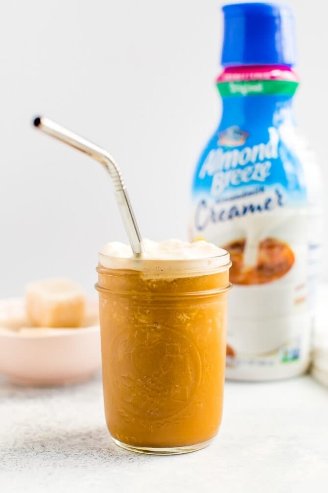 Almond Breeze almondmilk creamer bottle next to a frothy glass of blended cold brew and creamer.